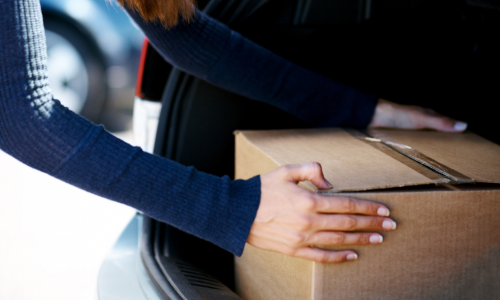 A cardboard box being put in a car trunk.